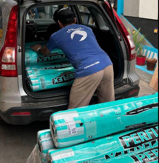 Empleado del corralón cargando rollos de membrana en el baúl del auto de un cliente
